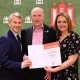 HFV-Präsident Christian Okun, Thomas Grage und HFV-Vizepräsidentin Kathrin Behn stehen gemeinsam vor einem Hintergrund mit HFV-Logos und zeigen eine Urkunde